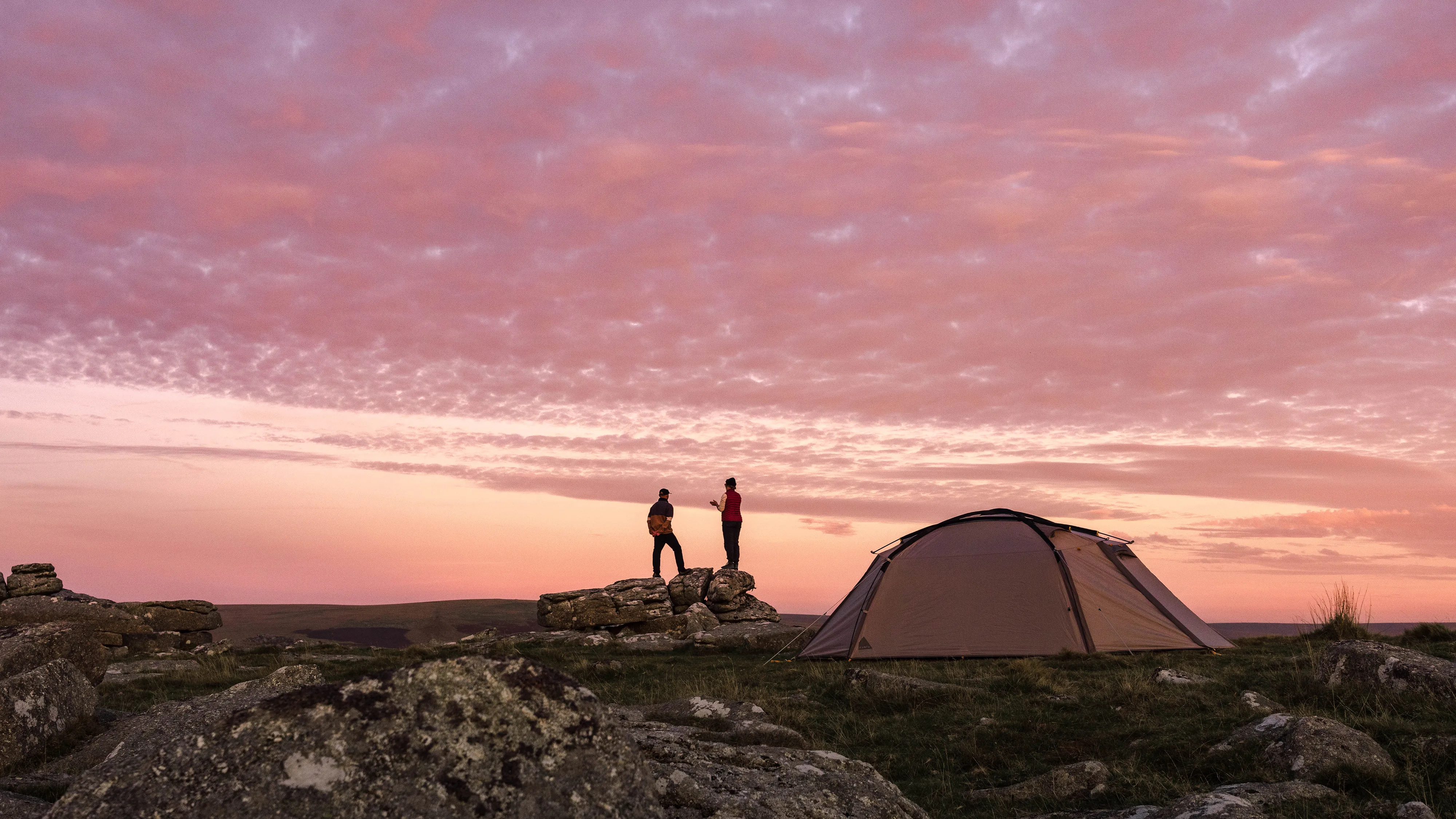 A couple looking out over a pink sunset with a Kampa tent in the foreground